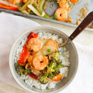 shrimp and vegetable stir fry served over rice in a white bowl.