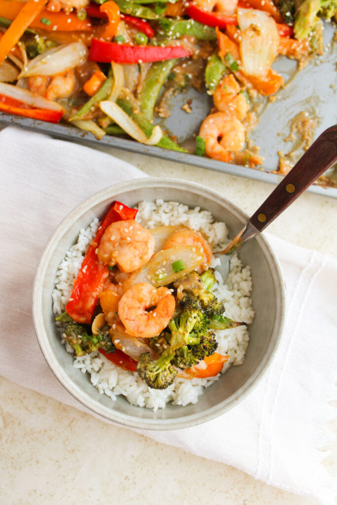 shrimp and vegetable stir fry served over rice in a white bowl.