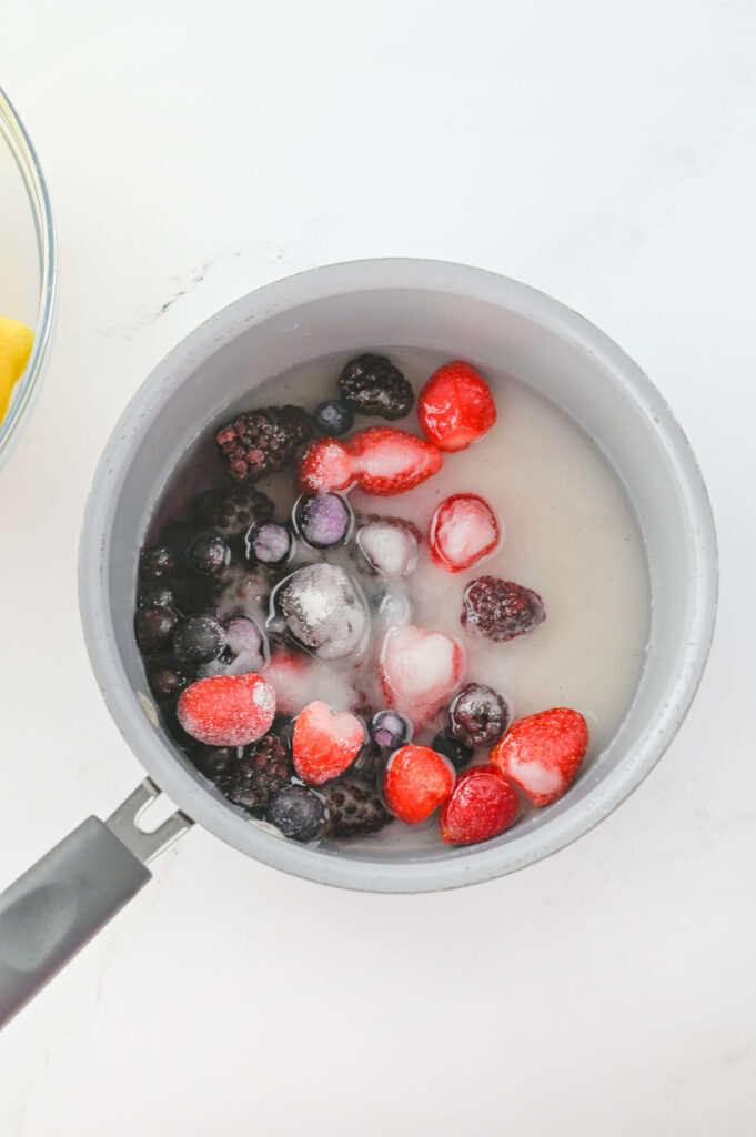 strawberries, blueberries, and blackberries combined with sugar in a sauce pan.