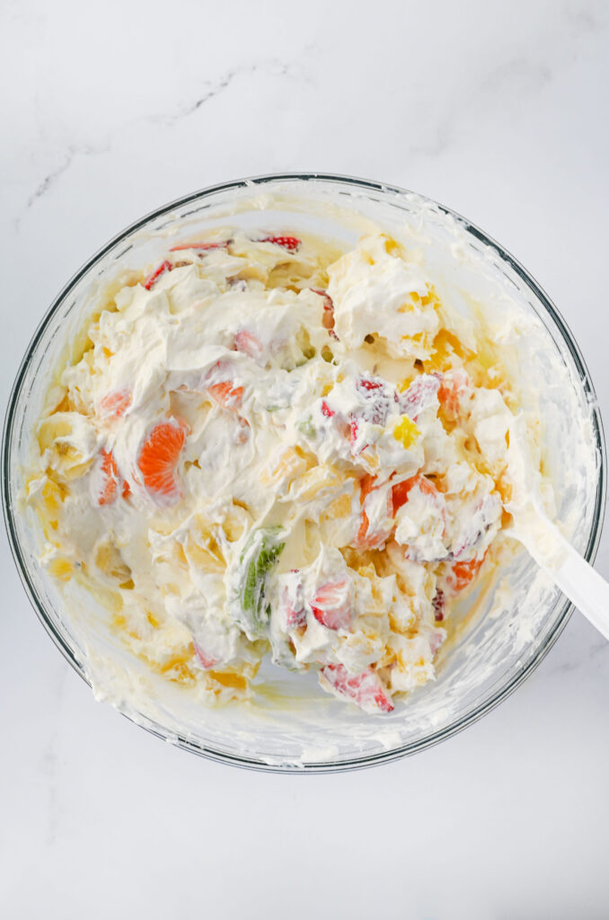 Todos os ingredientes combinados em uma tigela de vidro para fazer salada de cheesecake havaiana.