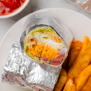 a California burrito served with fries and salsa on a white plate.