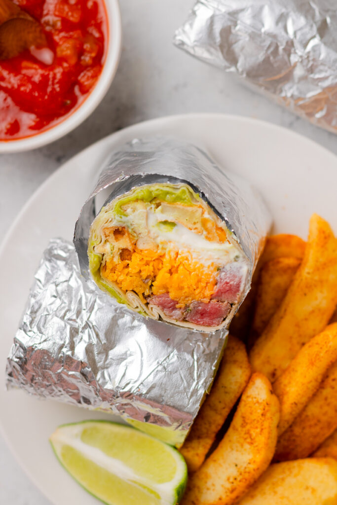 a California burrito served with fries and salsa on a white plate.