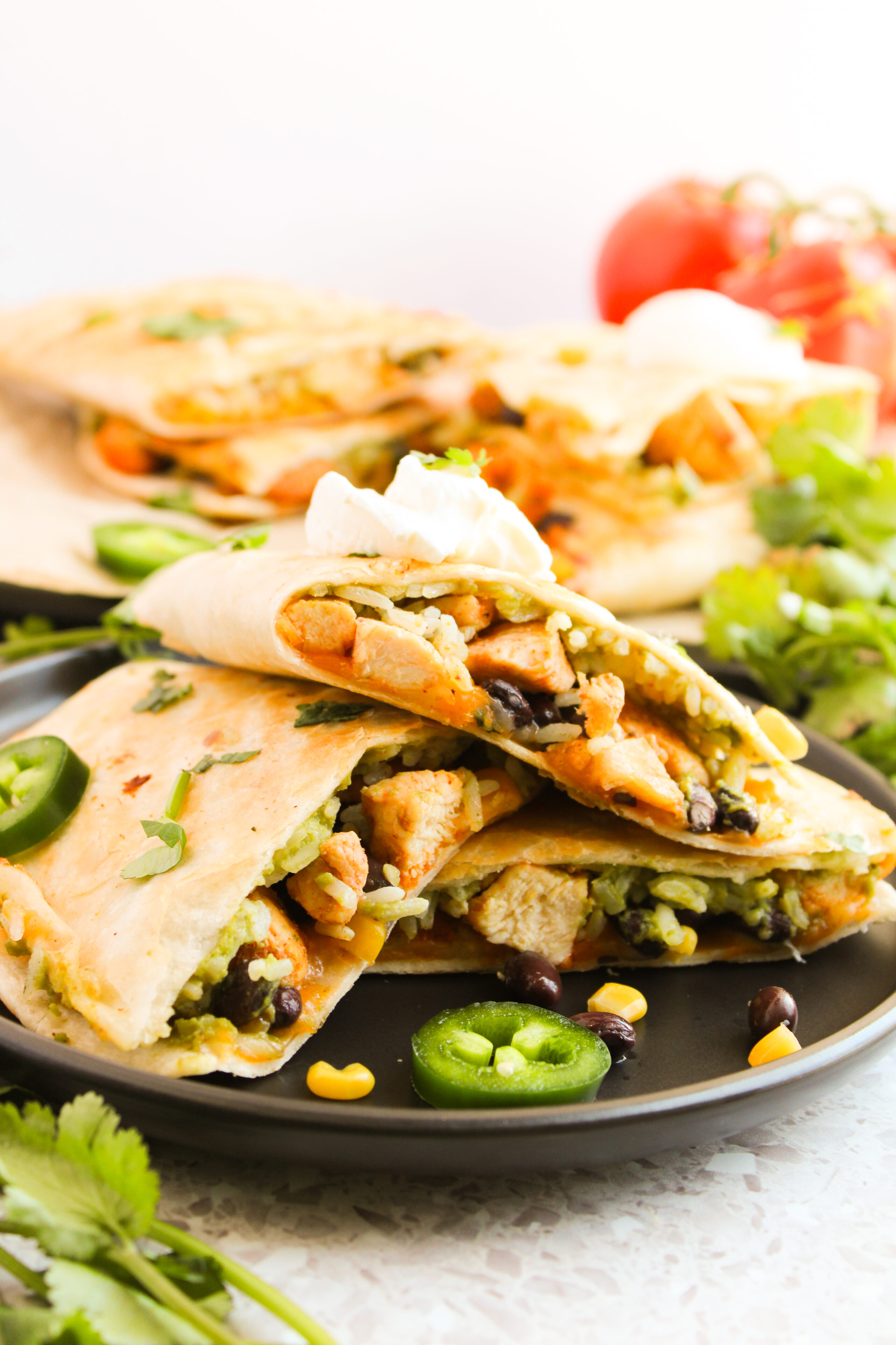 a southwestern chicken quesadilla on a black plate with sour cream and jalapenos.