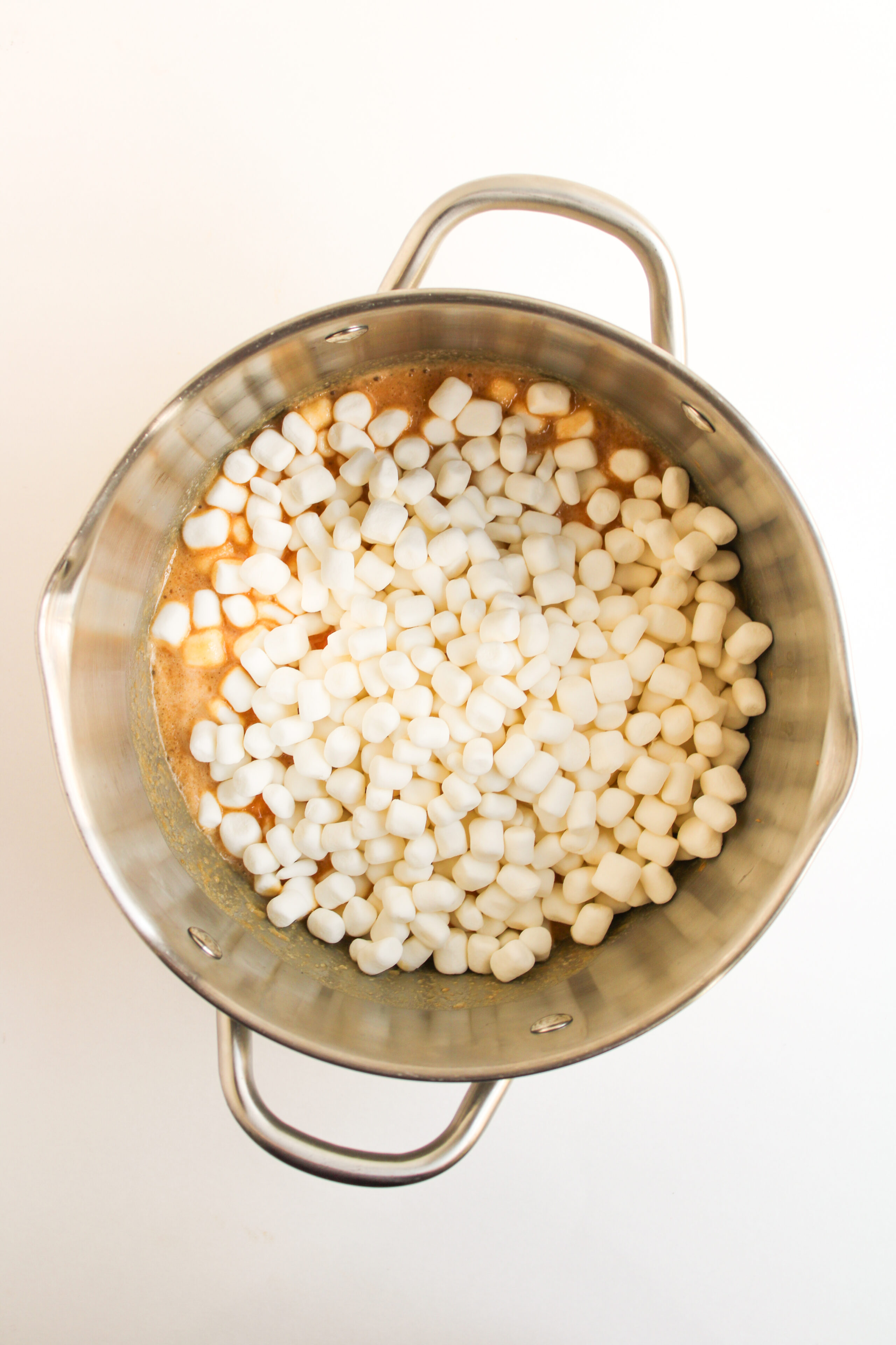 mini marshmallows added to a creamy peanut butter mixture in a saucepan.