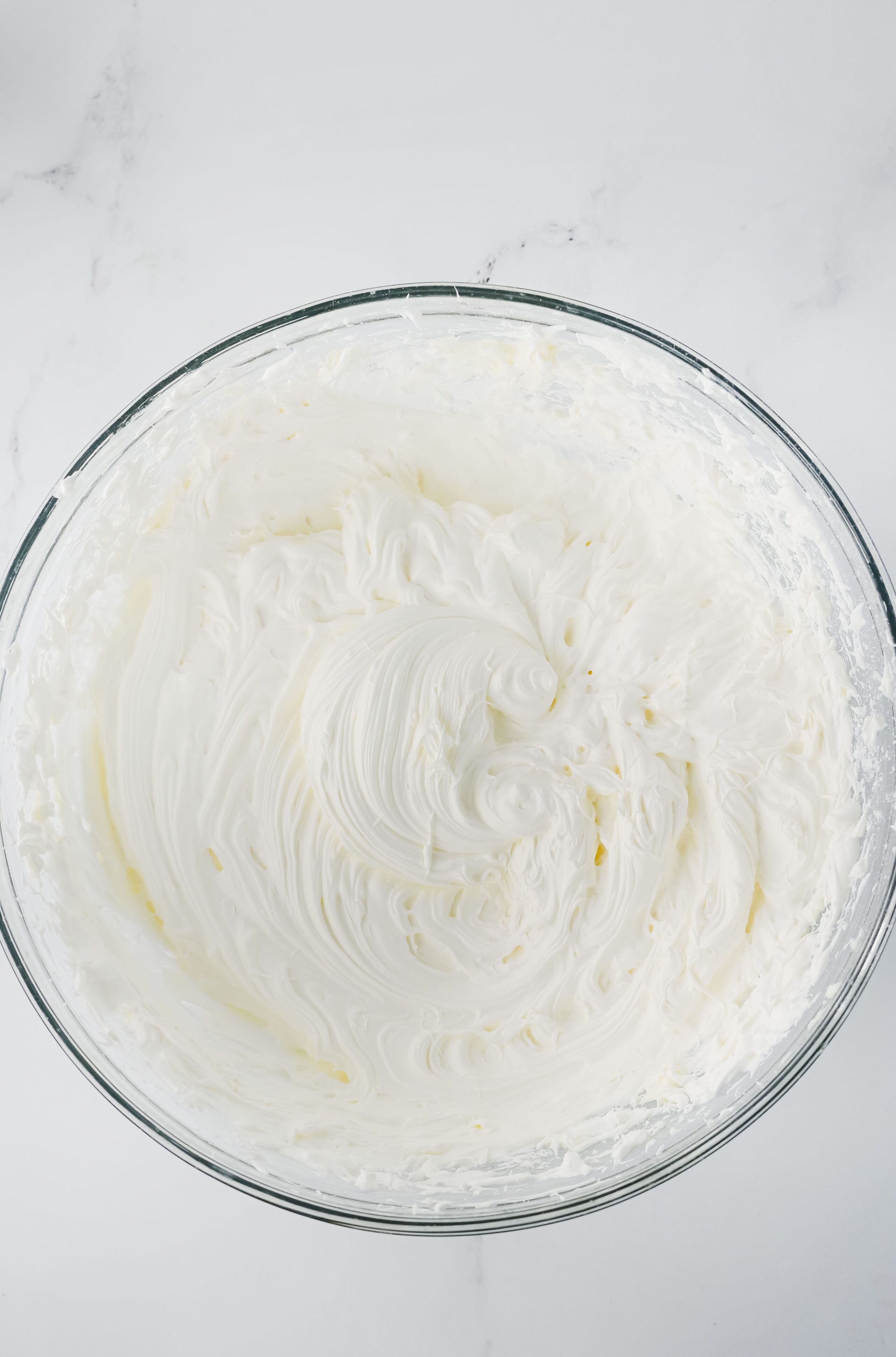 cool whip folded into a cream cheese mixture in a glass mixing bowl.