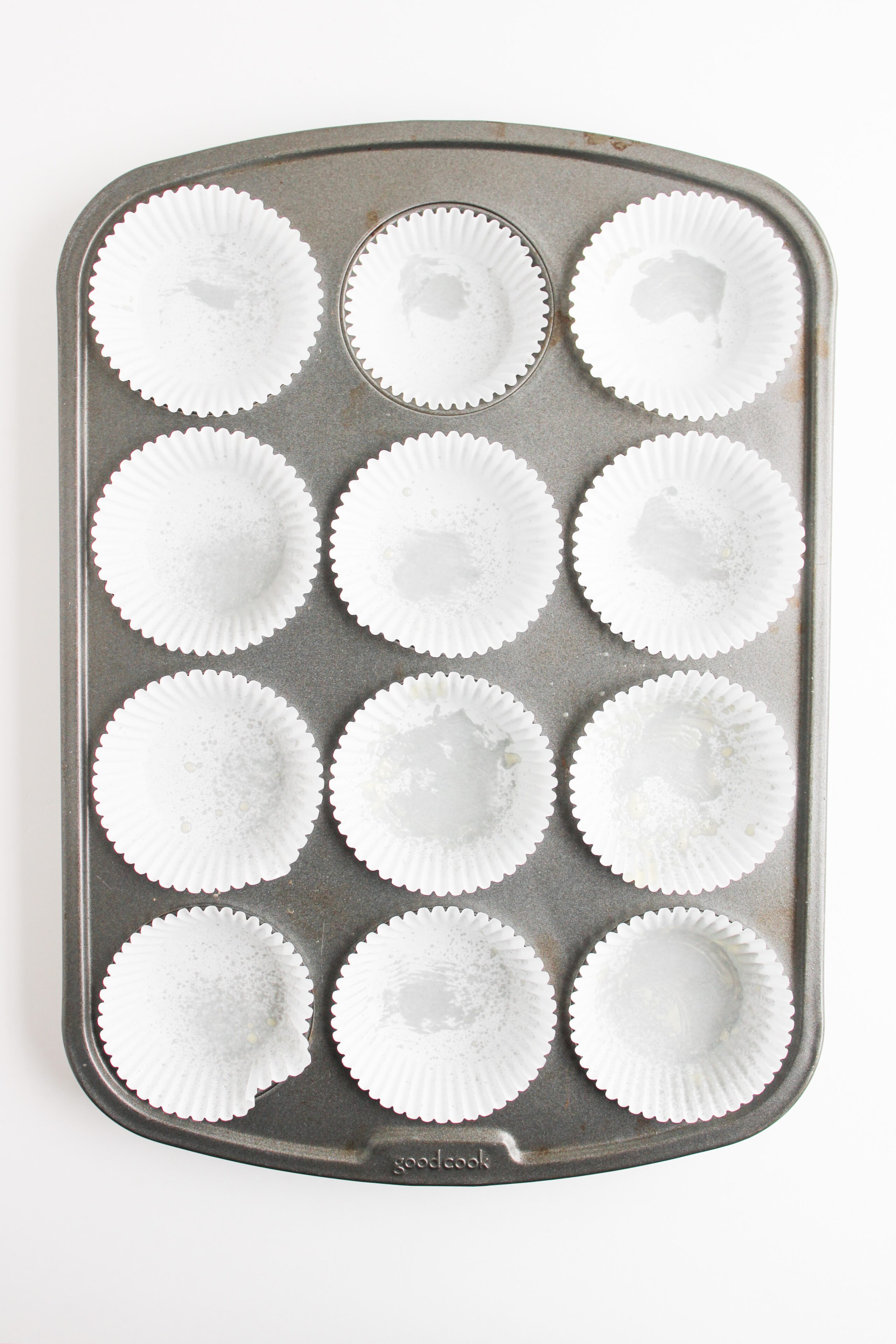 Metal muffin pan lined with white paper cupcake liners, ready for batter to be poured.