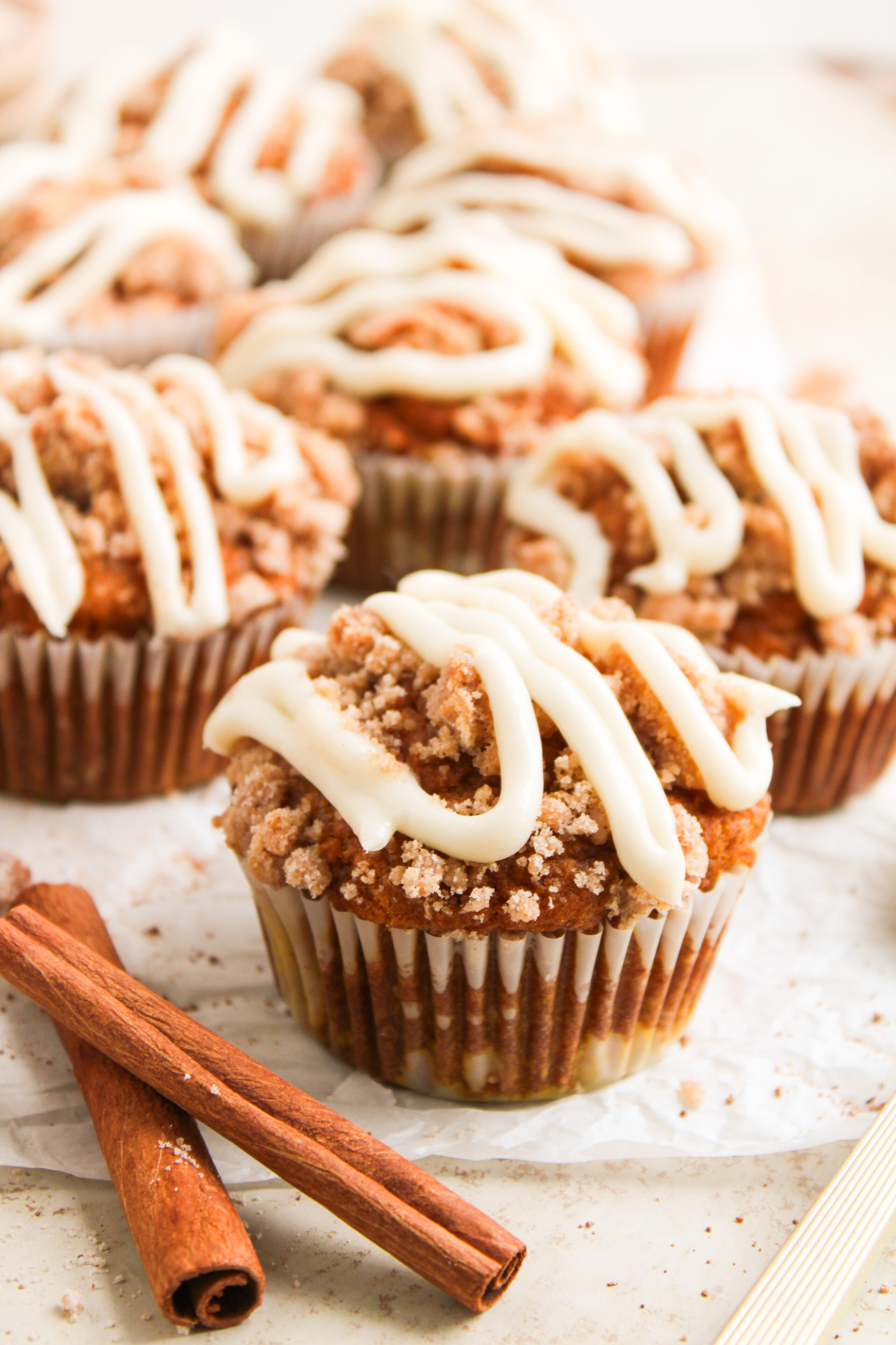 Close-up of golden-brown pumpkin spice muffins with creamy white cream cheese frosting melting slightly on top.
