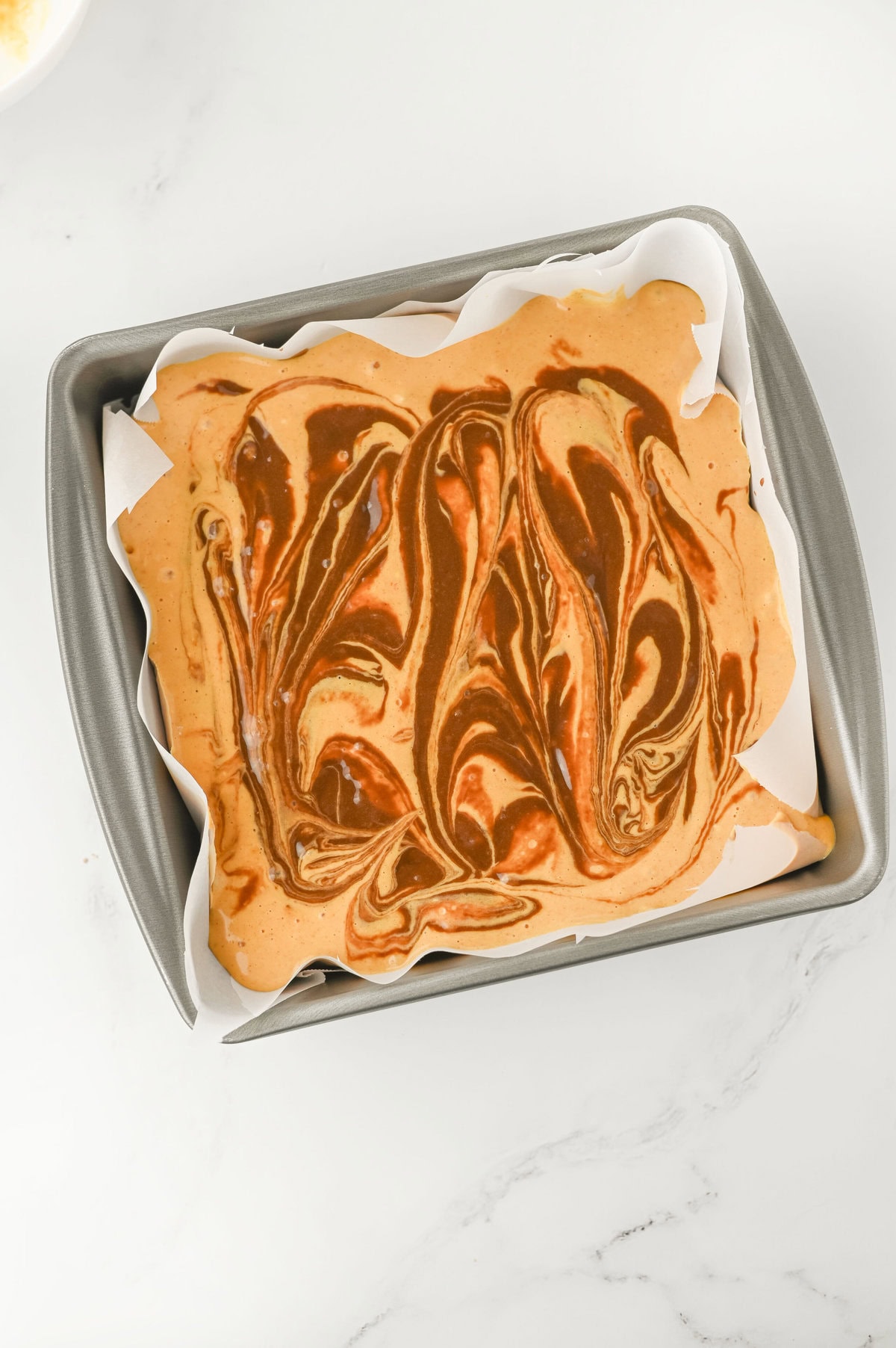 Using a knife to swirl pumpkin cheesecake mixture into brownie batter for pumpkin spice brownies.