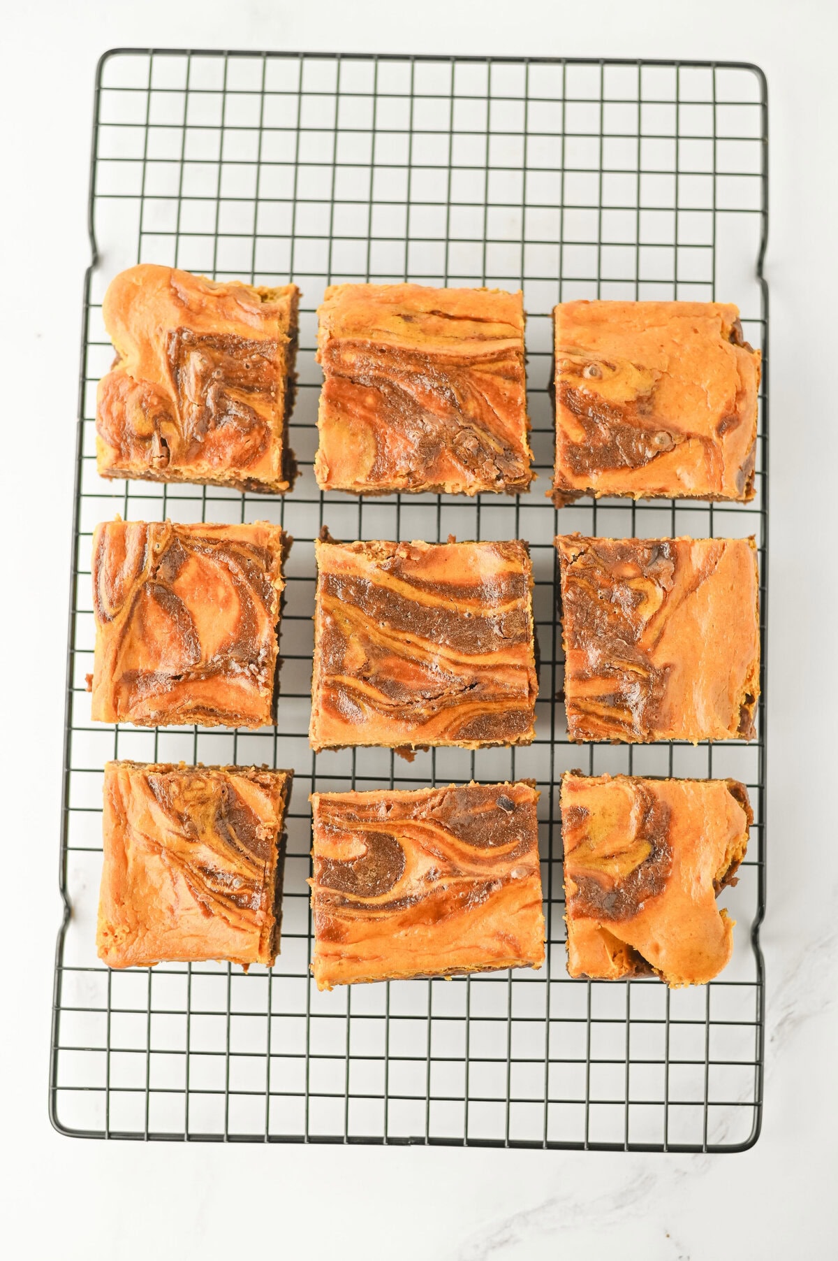 baked pumpkin brownies with a cream cheese swirl cooking on a wire rack.