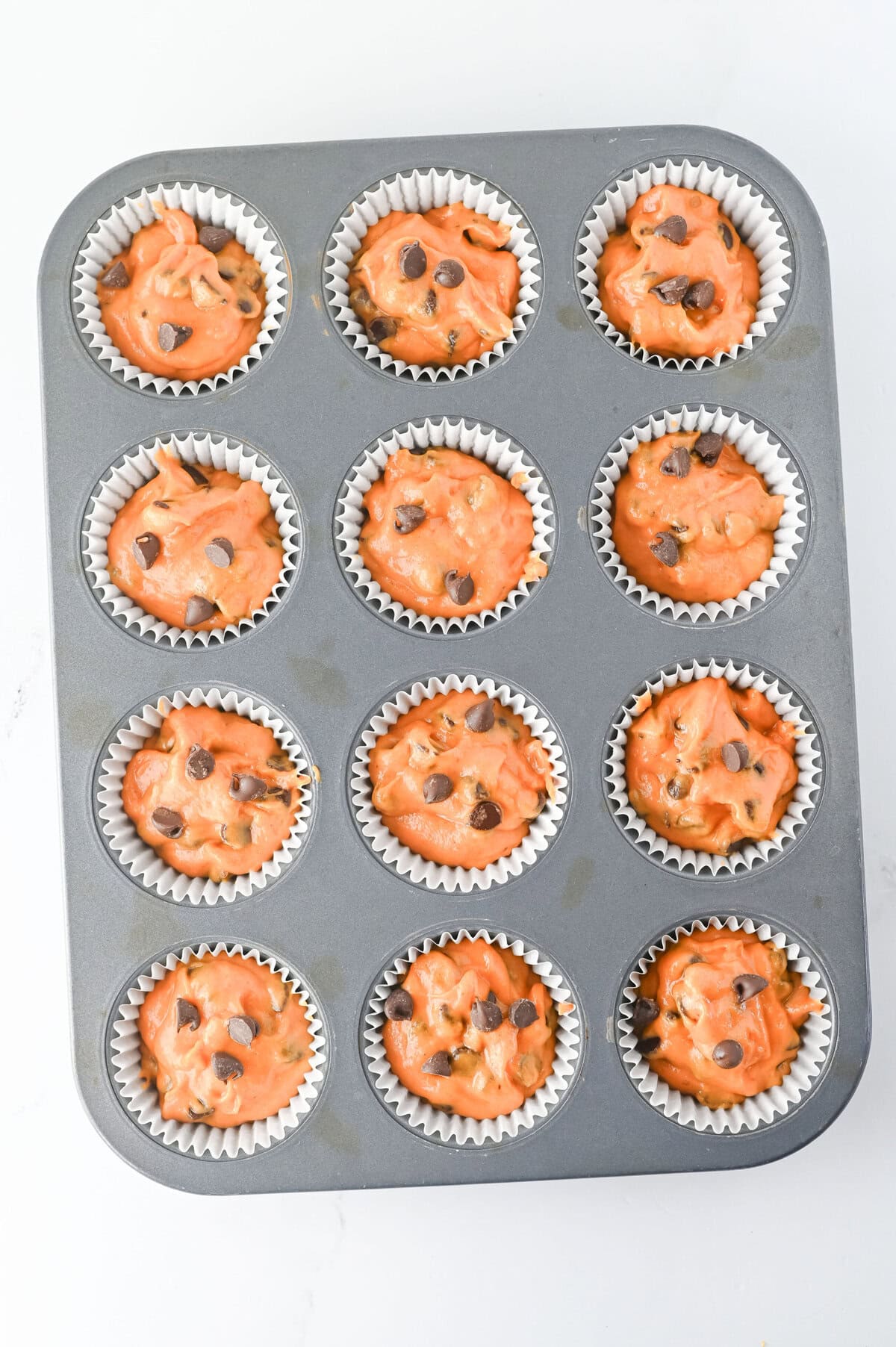 pumpkin chocolate chip muffin batter divided into paper lined muffin cups.