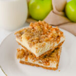 stacked apple cinnamon cheesecake bars on a white serving plate.
