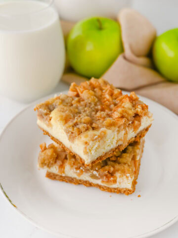 stacked apple cinnamon cheesecake bars on a white serving plate.