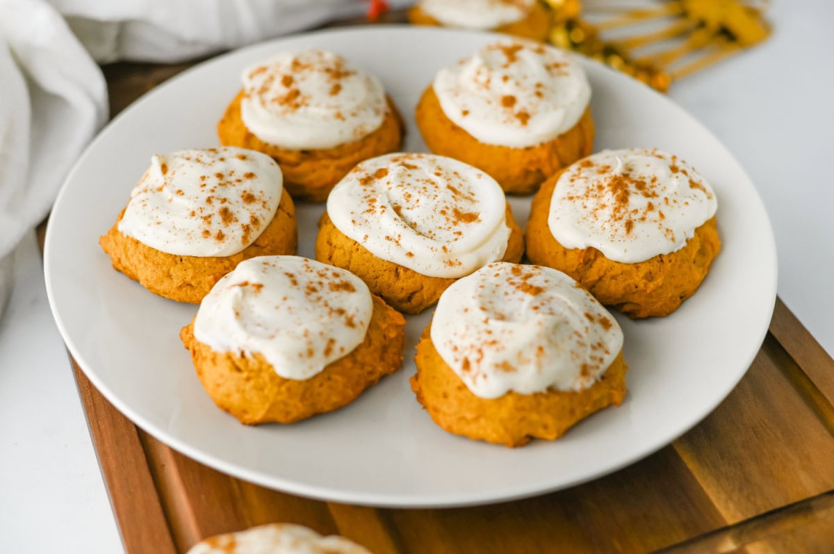 Chewy pumpkin cookie topped with creamy cream cheese frosting on a white plate.