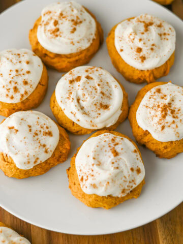 Soft pumpkin cookies with cream cheese frosting on a white plate.