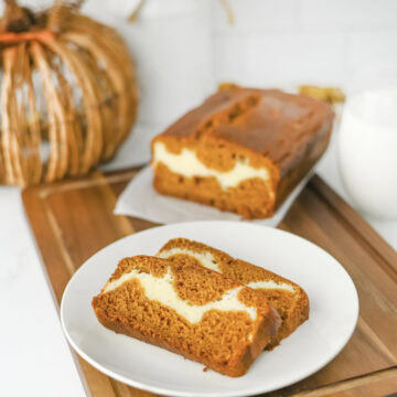 sliced pumpkin cream cheese bread on a white plate with a full loaf behind it.