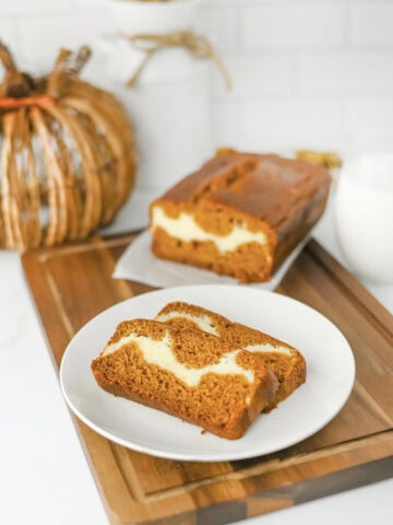 sliced pumpkin cream cheese bread on a white plate with a full loaf behind it.