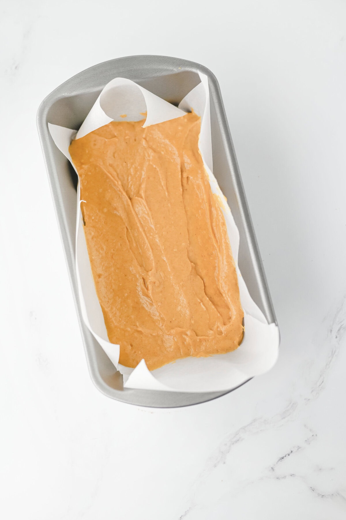 pumpkin bread batter in a loaf pan lined with parchment paper.