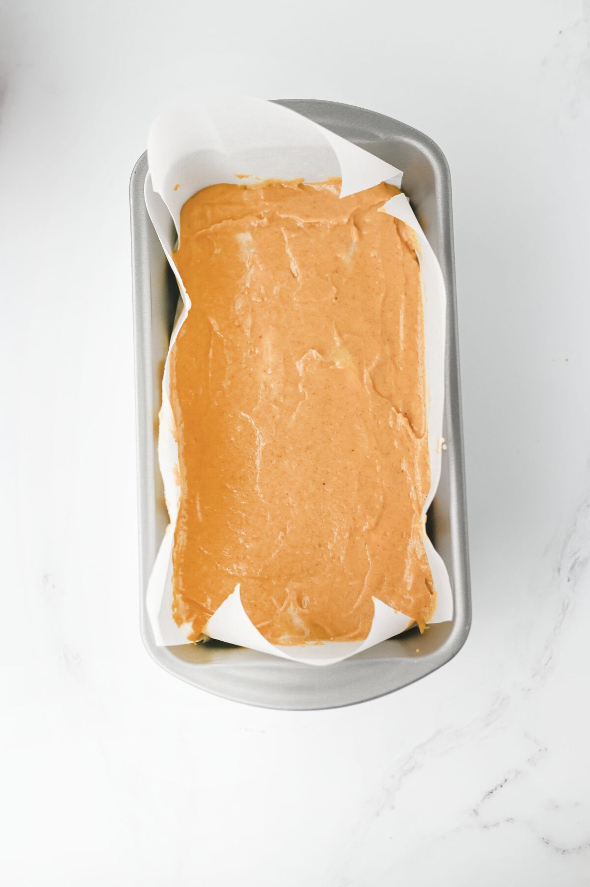 pumpkin batter on top of a cream cheese layer in a loaf pan.