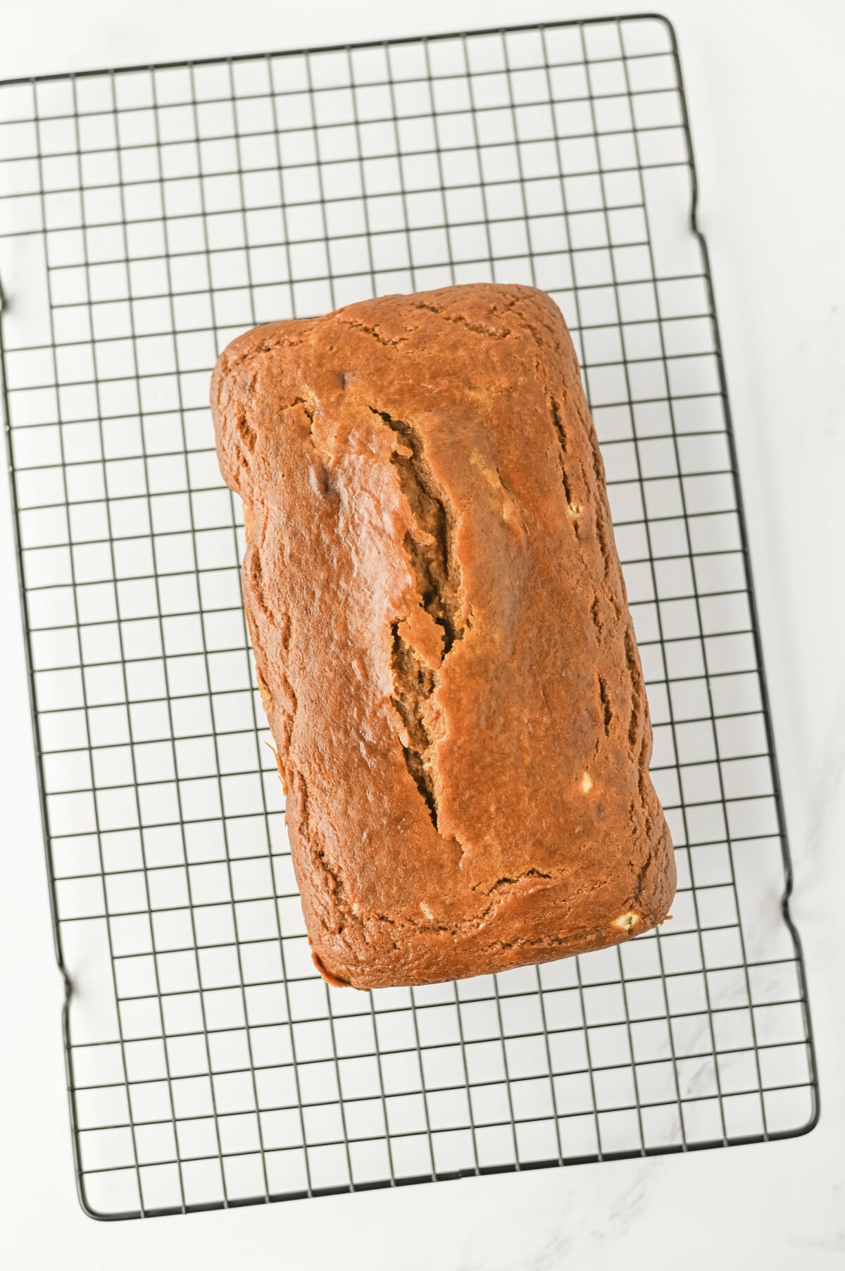 a baked loaf of pumpkin cream cheese bread on a wire cooling rack.