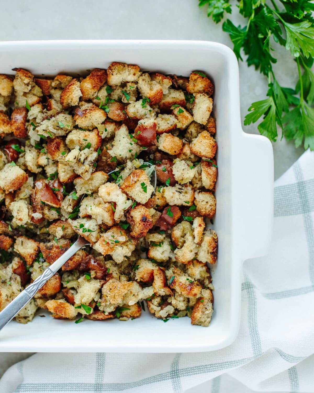 Thanksgiving stuffing baked in a white baking dish and served with a large spoon.