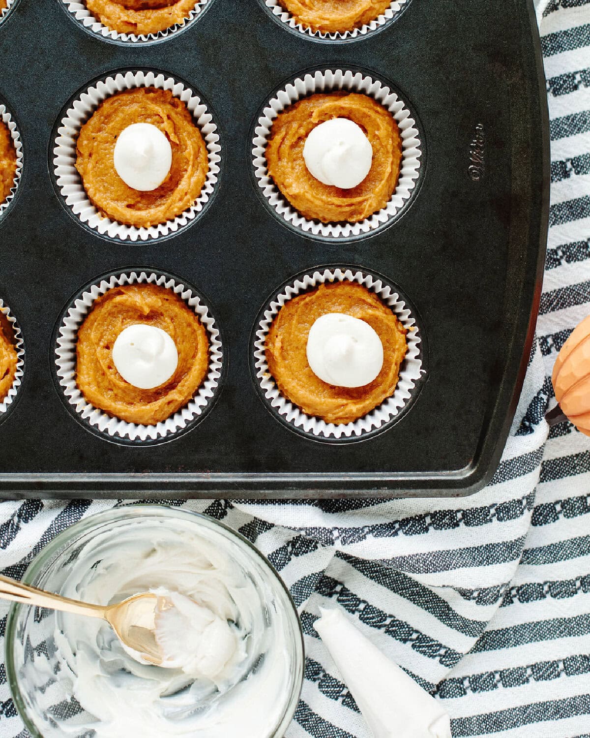 cream cheese filling piped into the center of pumpkin muffins in a paper lined muffin tray.