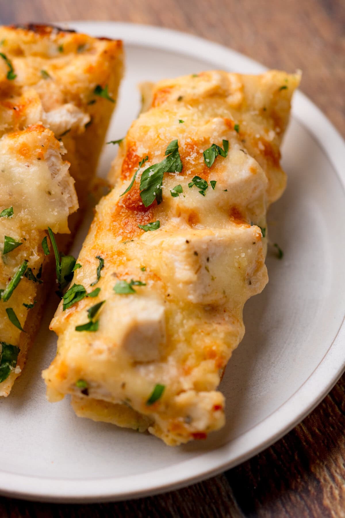 melted cheese on top of chicken, creamy sauce, and cheese on a white plate.