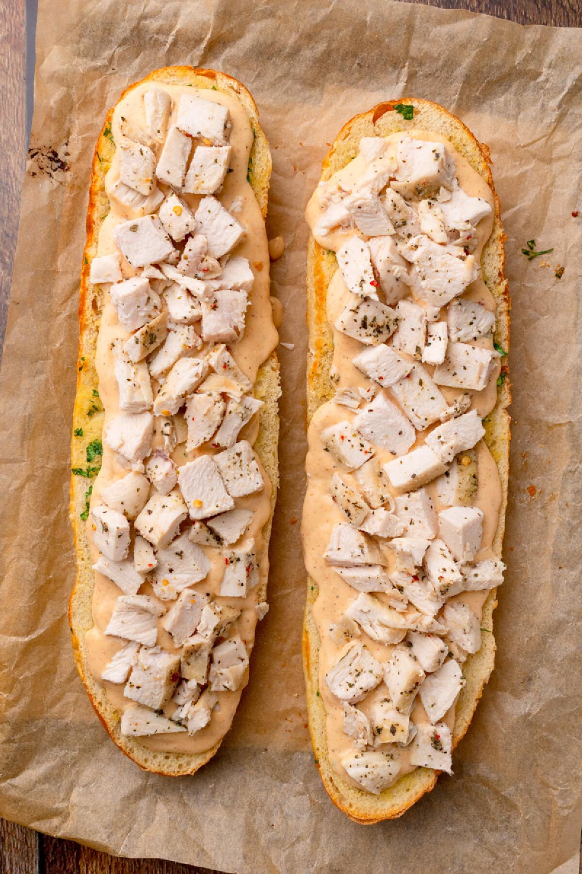 cooked chopped chicken sprinkled on top of Alfredo sauce on garlic bread.