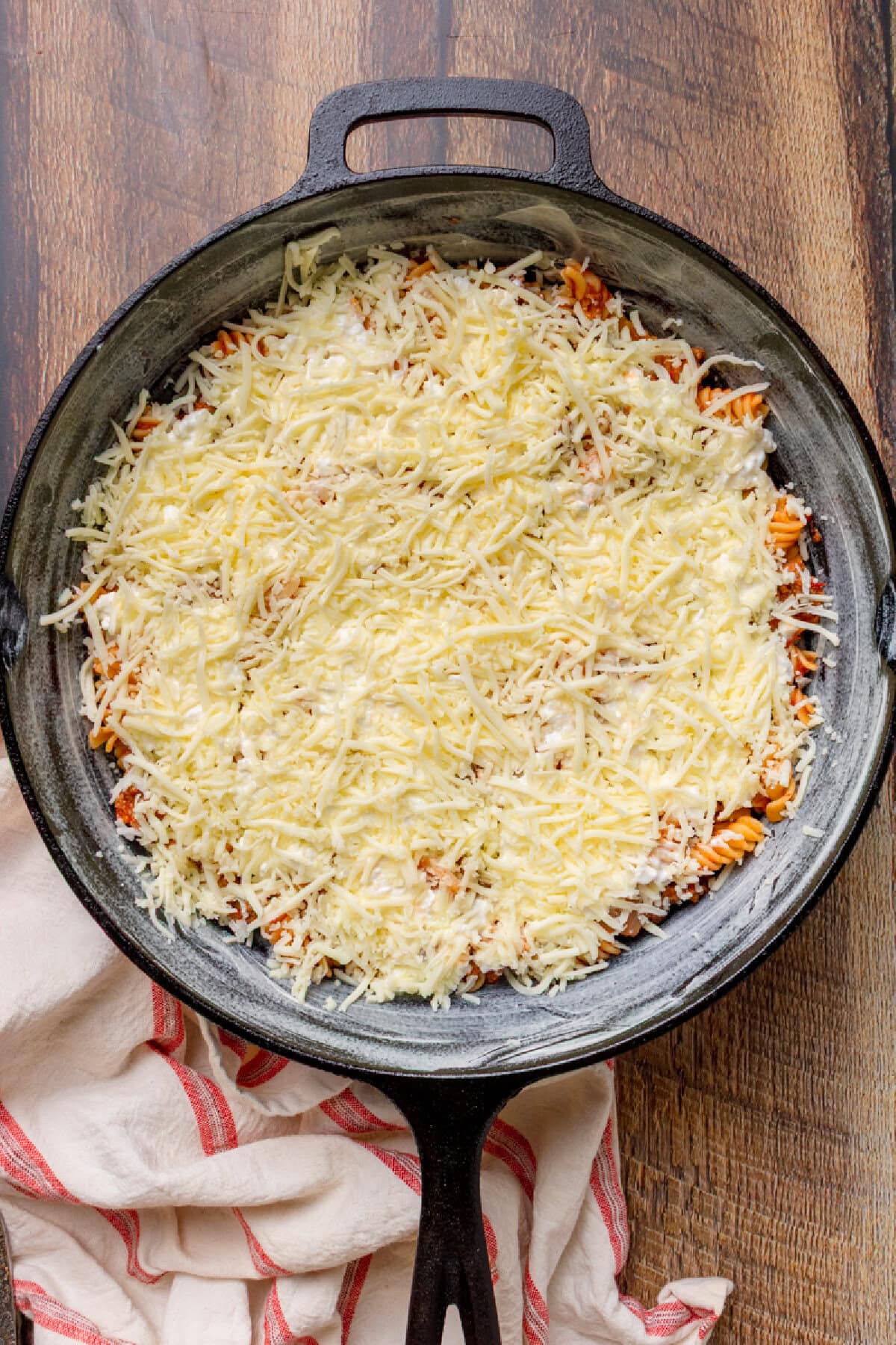 shredded mozzarella cheese on top of cooked pasta with a meat sauce in a skillet.