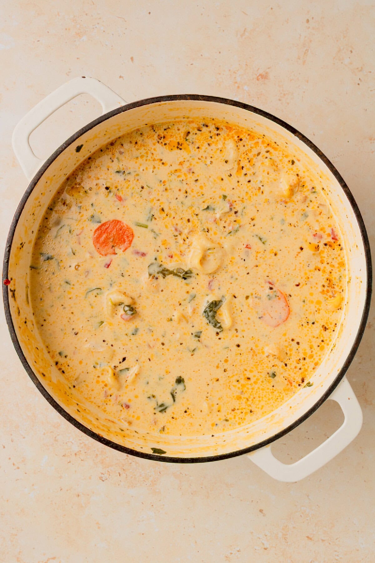 creamy sausage and tortellini soup in a white Dutch oven.