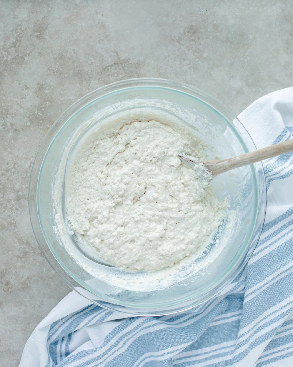 dough combined in a glass mixing bowl with a wood spoon.