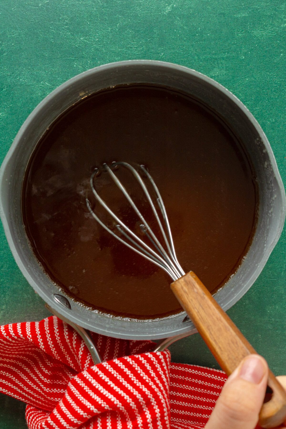 a chocolate glaze simmering in a saucepan with a whisk.