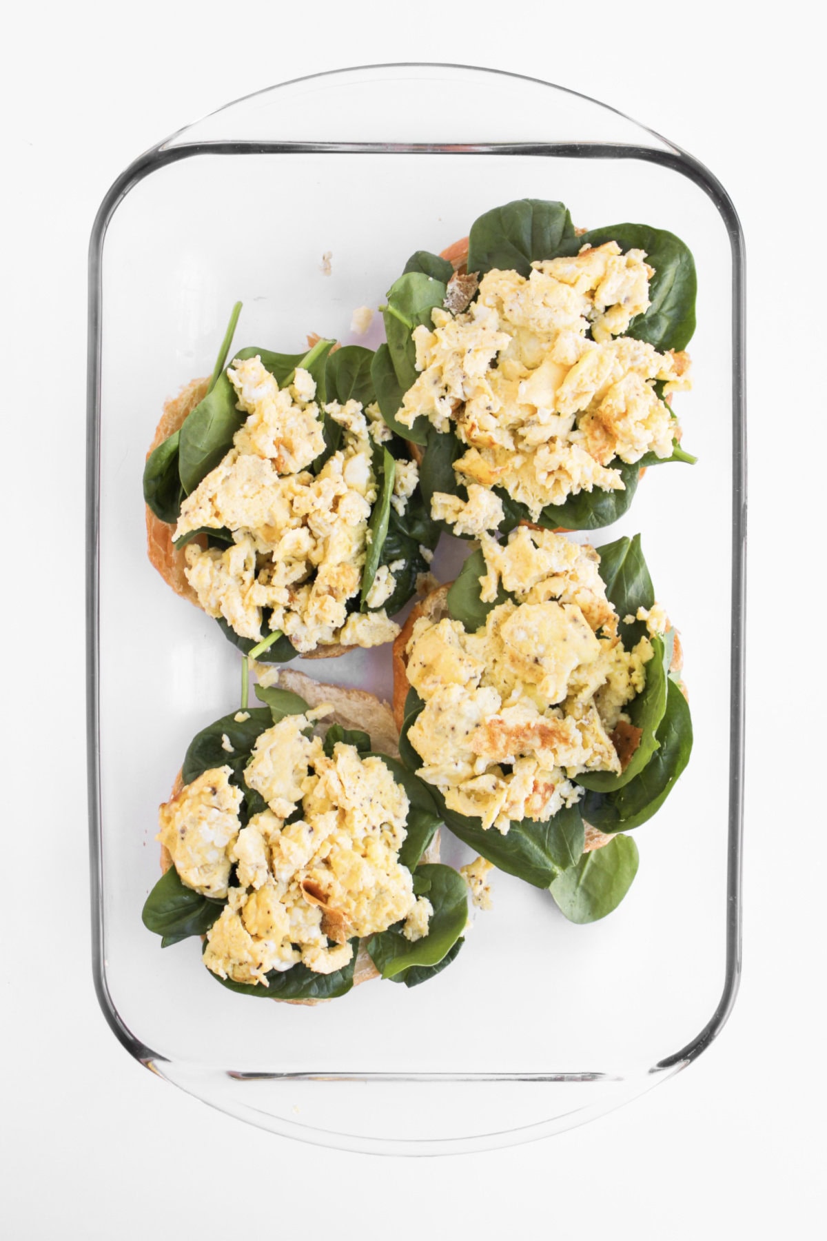 scrambled eggs placed on top of spinach and croissant bottoms in a baking dish.