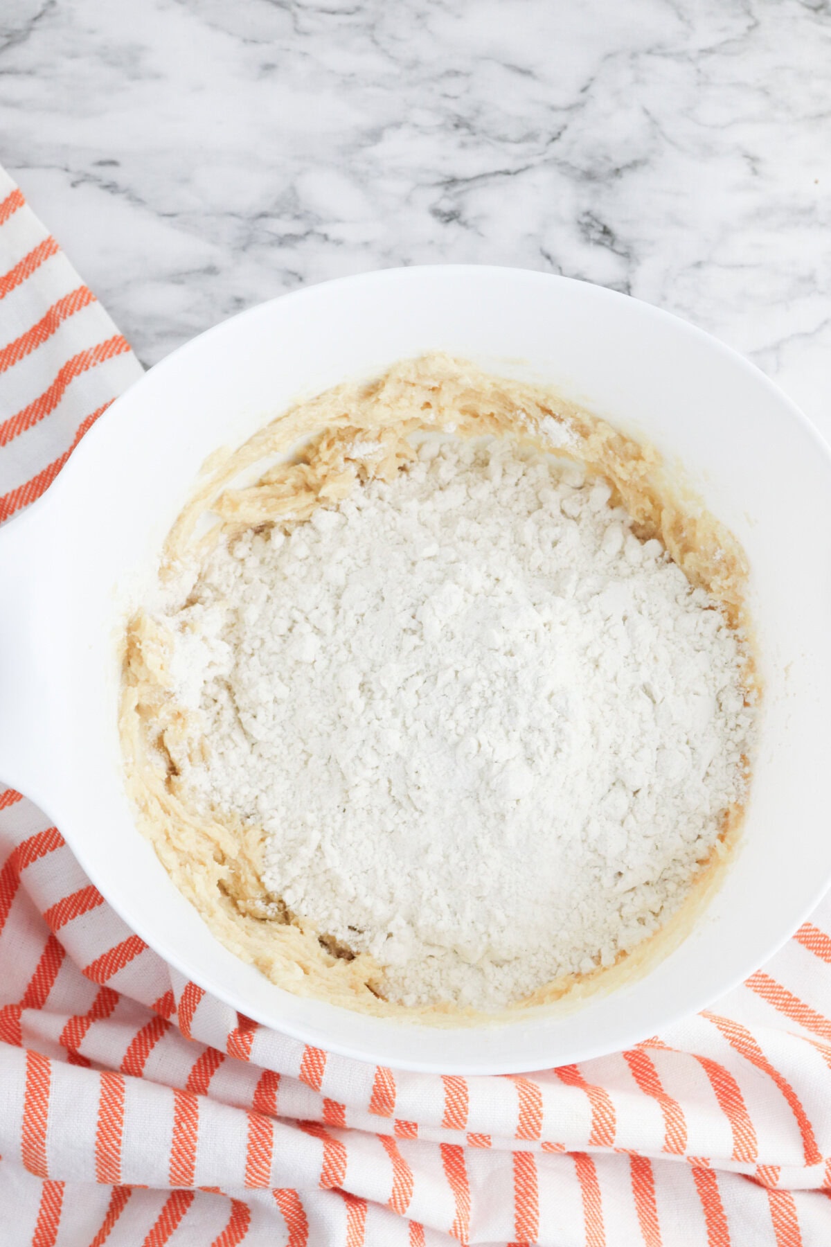 dry ingredients added to creamed butter mixture in a white mixing bowl.