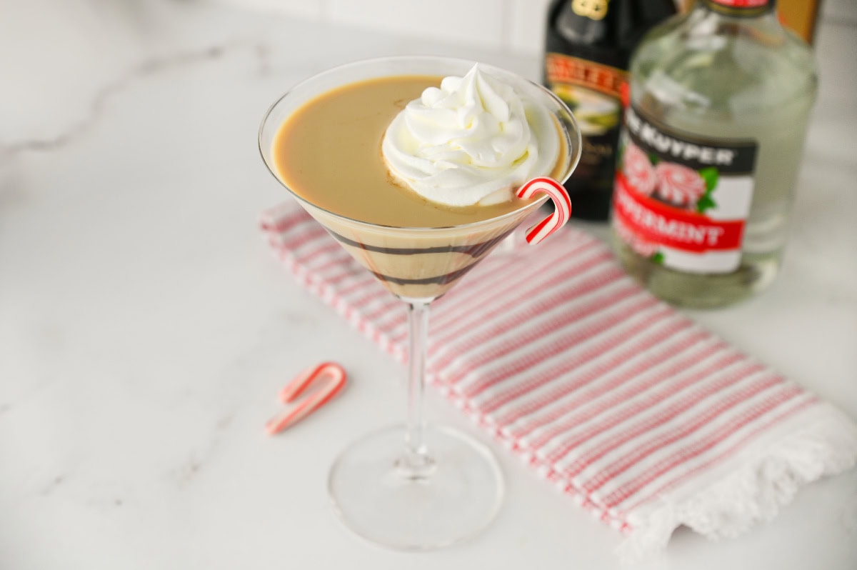 an up close look at a 3 ingredients Peppermint Martini garnished with whipped cream and a candy cane.