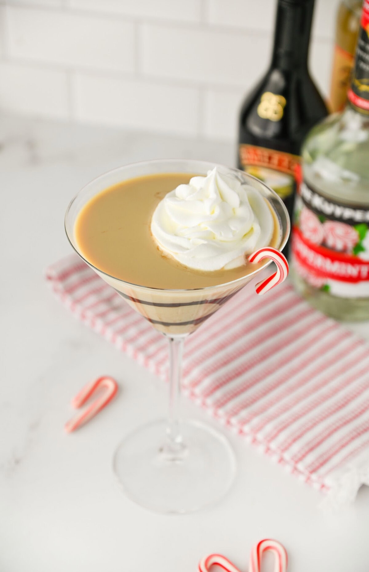 a Bailey's Peppermint Martini in a glass topped with whipped cream and a candy cane for garnish.