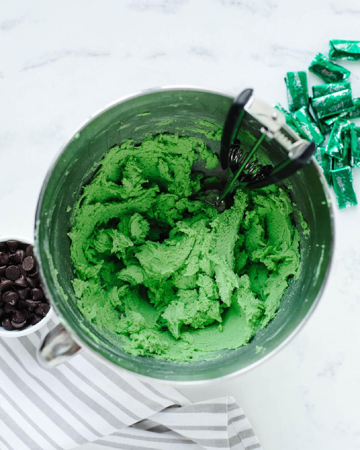 peppermint extract, egg, and green food coloring added to creamed butter and powdered sugar in a mixing bowl.