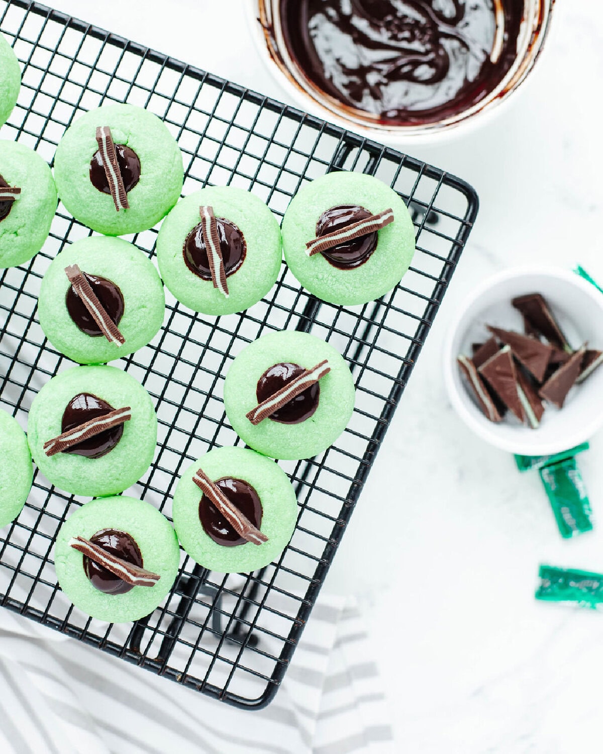 Chocolate Mint Thumbprint Cookies cooling on a wire rack with melted chocolate centers topped with Andes mints.