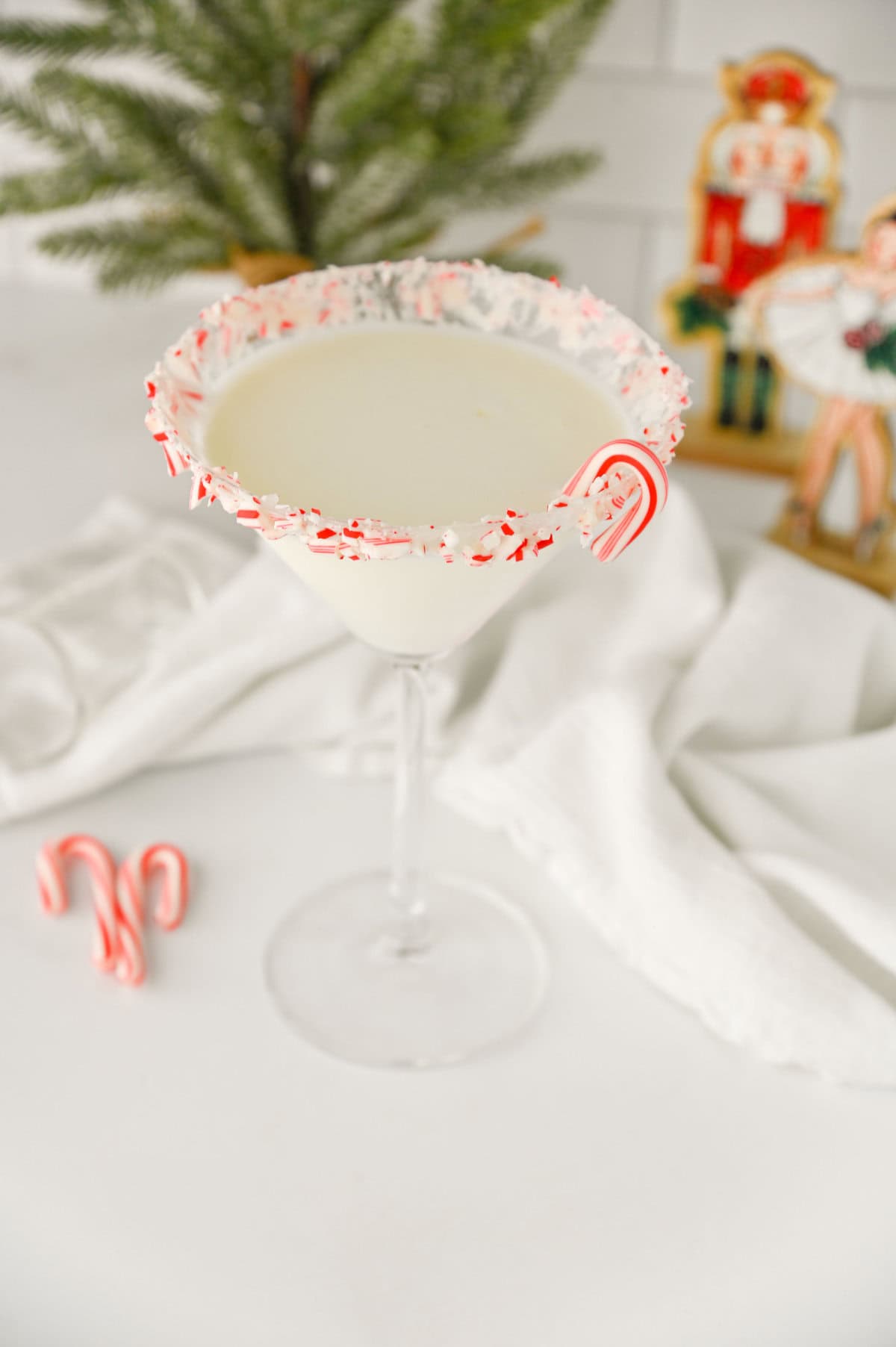 a festive candy cane rimmed martini glass filled with white chocolate peppermint martini and garnished with a mini candy cane.