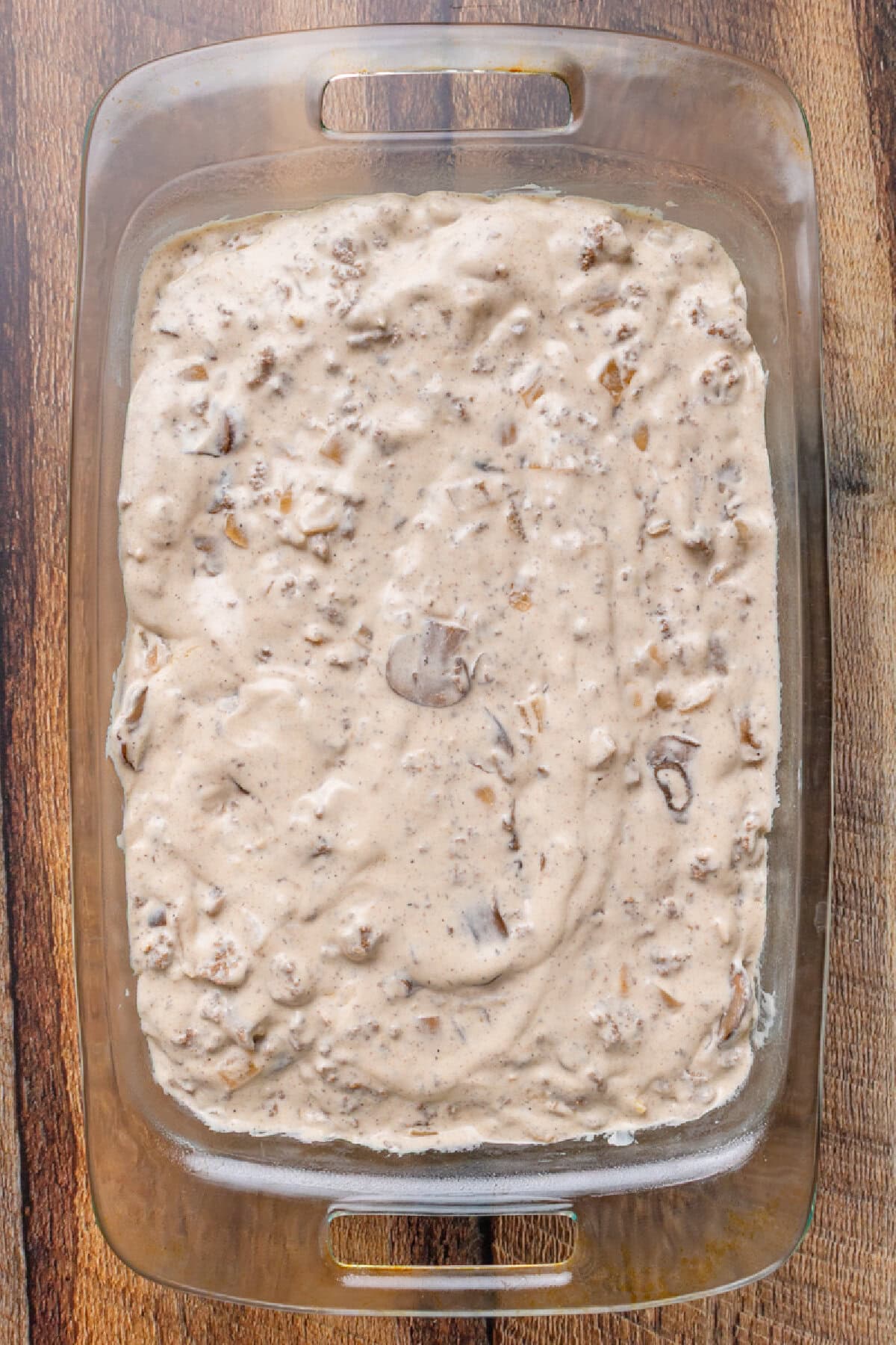 Creamy stroganoff mixture poured over cooked egg noodles in a baking dish.