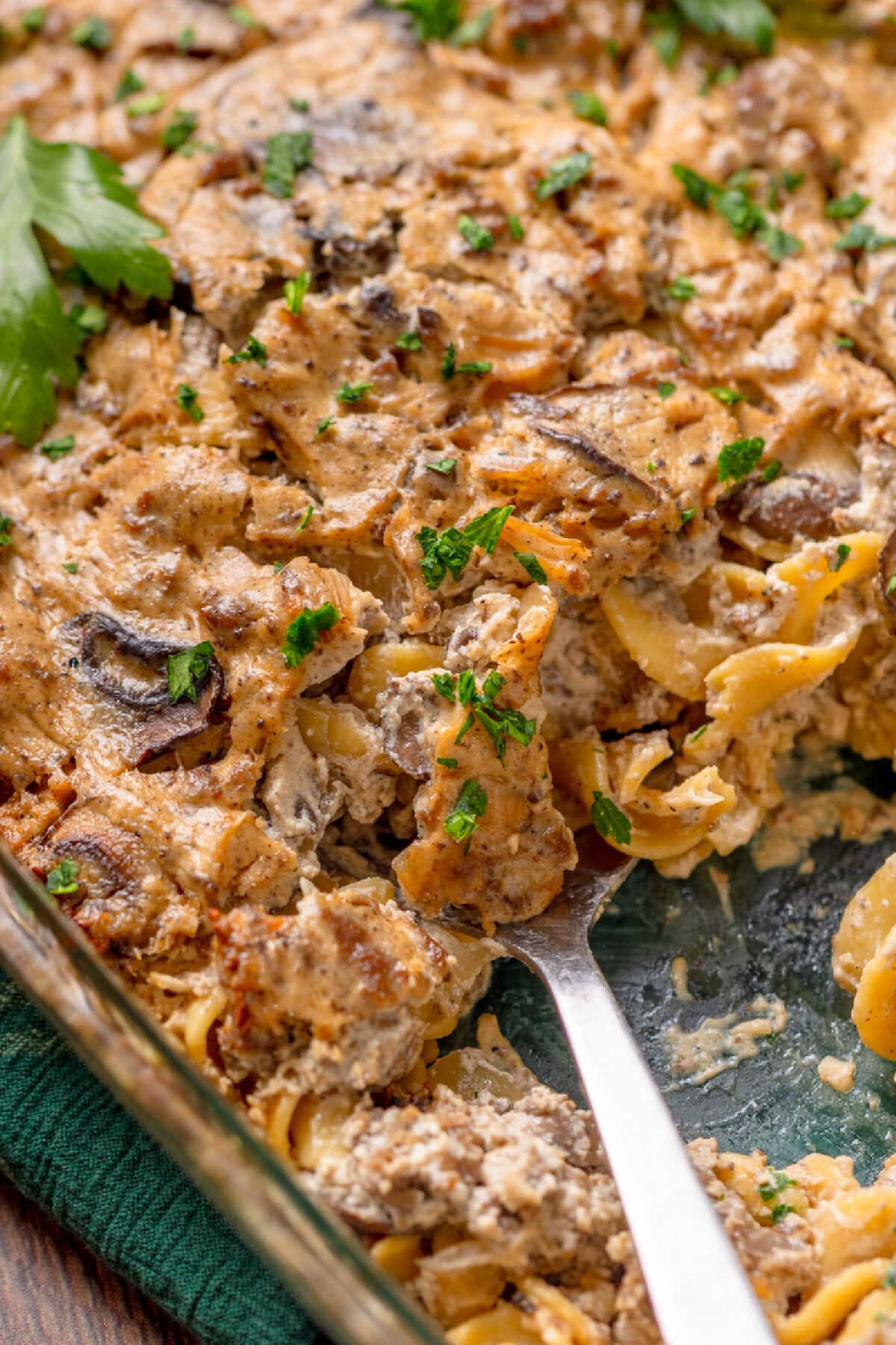 An up close view of creamy beef stroganoff casserole ready to serve with a large spoon.