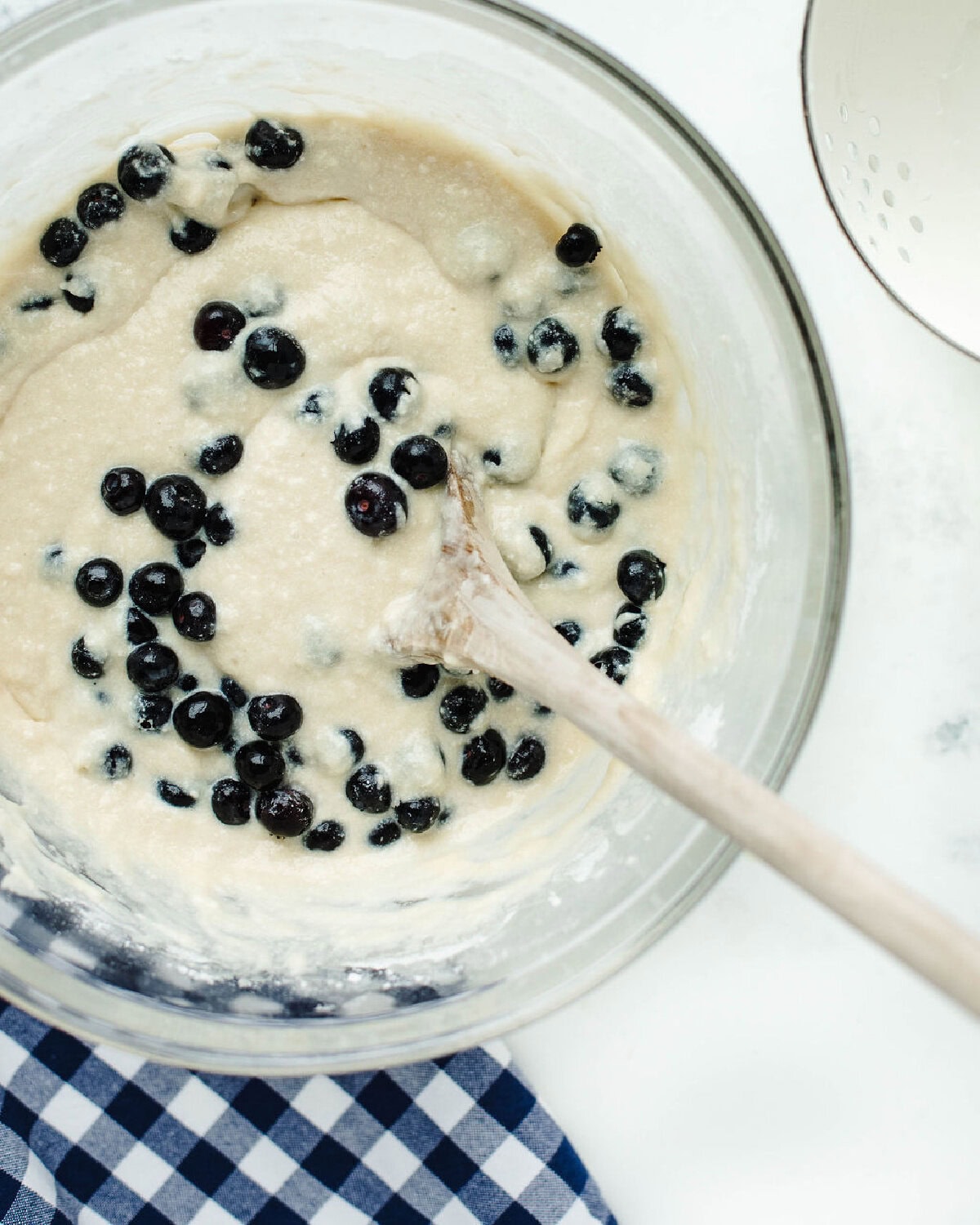 fresh blueberries folded into quick bread batter in a glass mixing bowl.