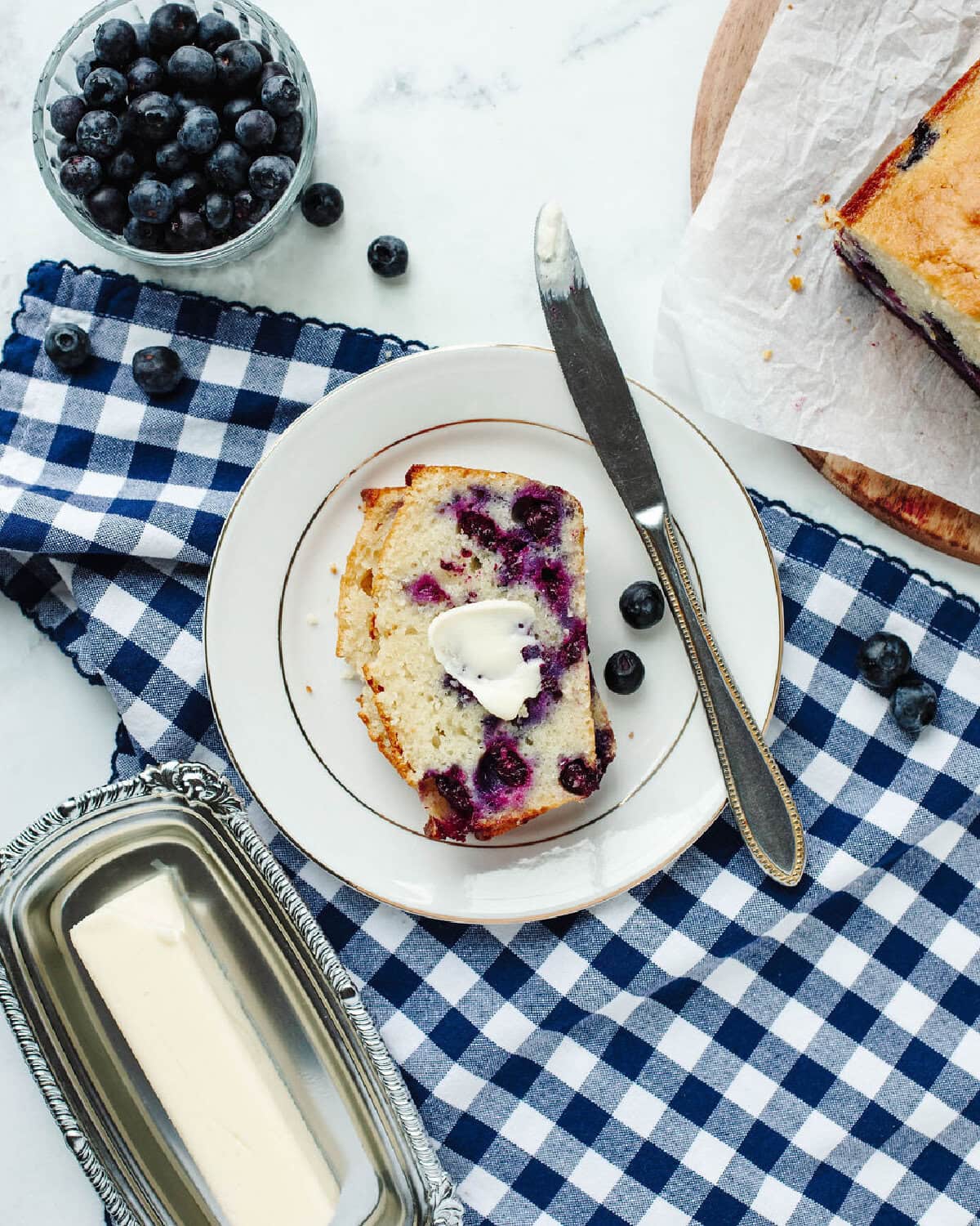 sliced blueberry bread with a spread of butter on a white plate with a knife.