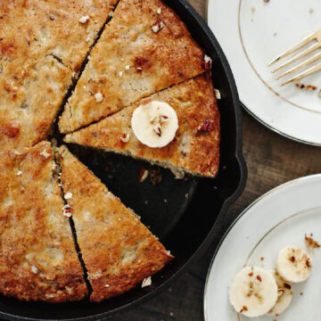Baked banana bread in a cast iron skillet with a slice removed.