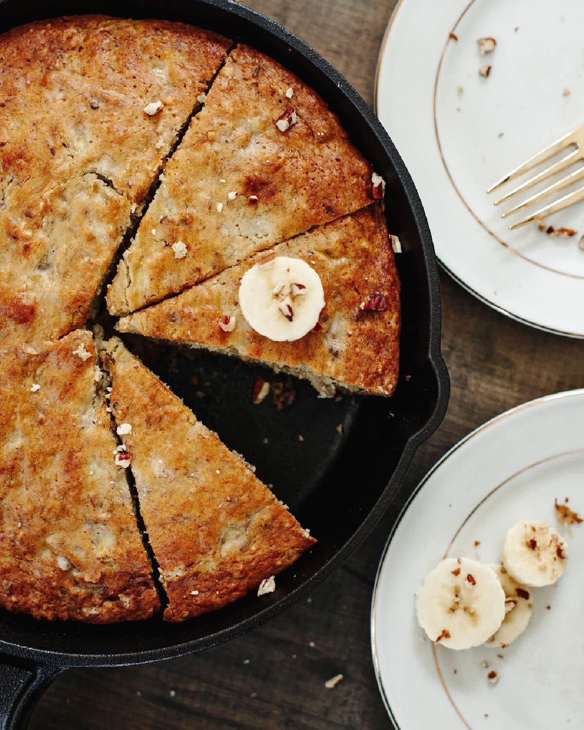 Baked banana bread in a cast iron skillet with a slice removed.