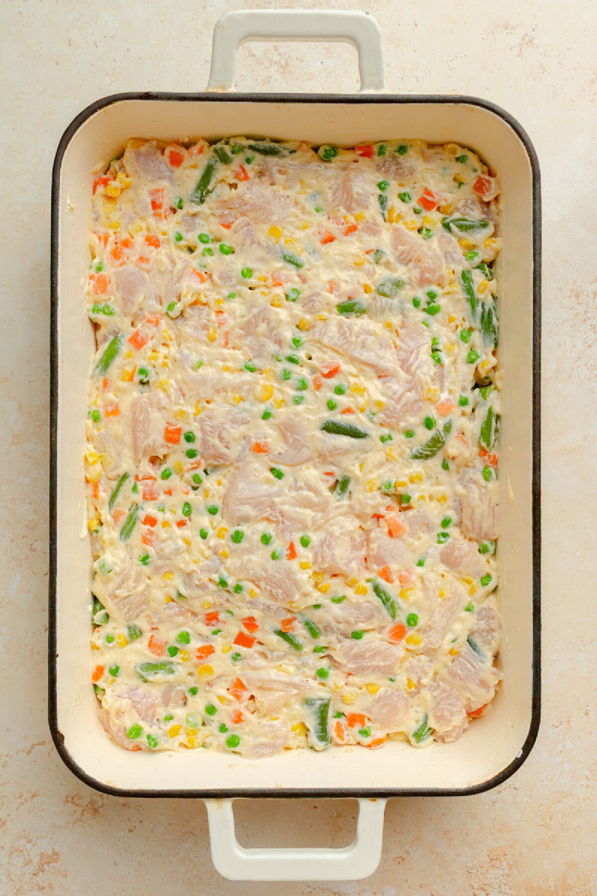 Chicken mixture spread into a baking dish before adding stuffing.