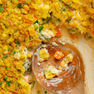A wooden spoon scooping out a serving of Chicken and Stuffing Casserole from a baking pan.