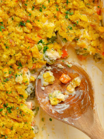 A wooden spoon scooping out a serving of Chicken and Stuffing Casserole from a baking pan.