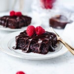 A slice of chocolate raspberry dump cake on a white plate with drizzled hot fudge and fresh raspberries.