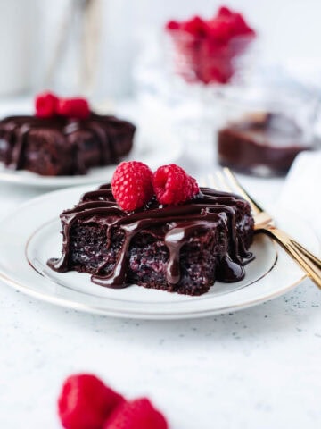A slice of chocolate raspberry dump cake on a white plate with drizzled hot fudge and fresh raspberries.