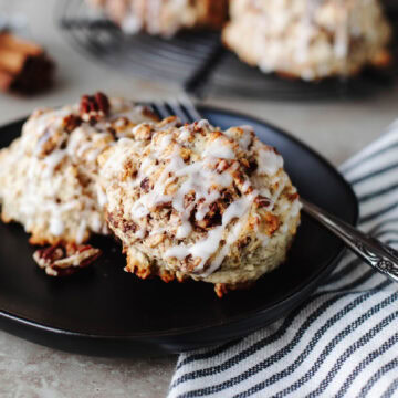 Cinnamon Bun Scones drizzled with icing on a black plate.